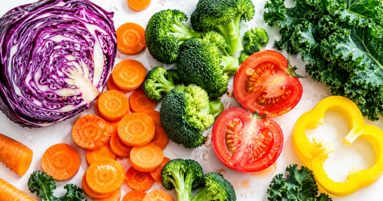 Halved red cabbage, carrot rounds, broccoli and tomato on dark stone under raking light